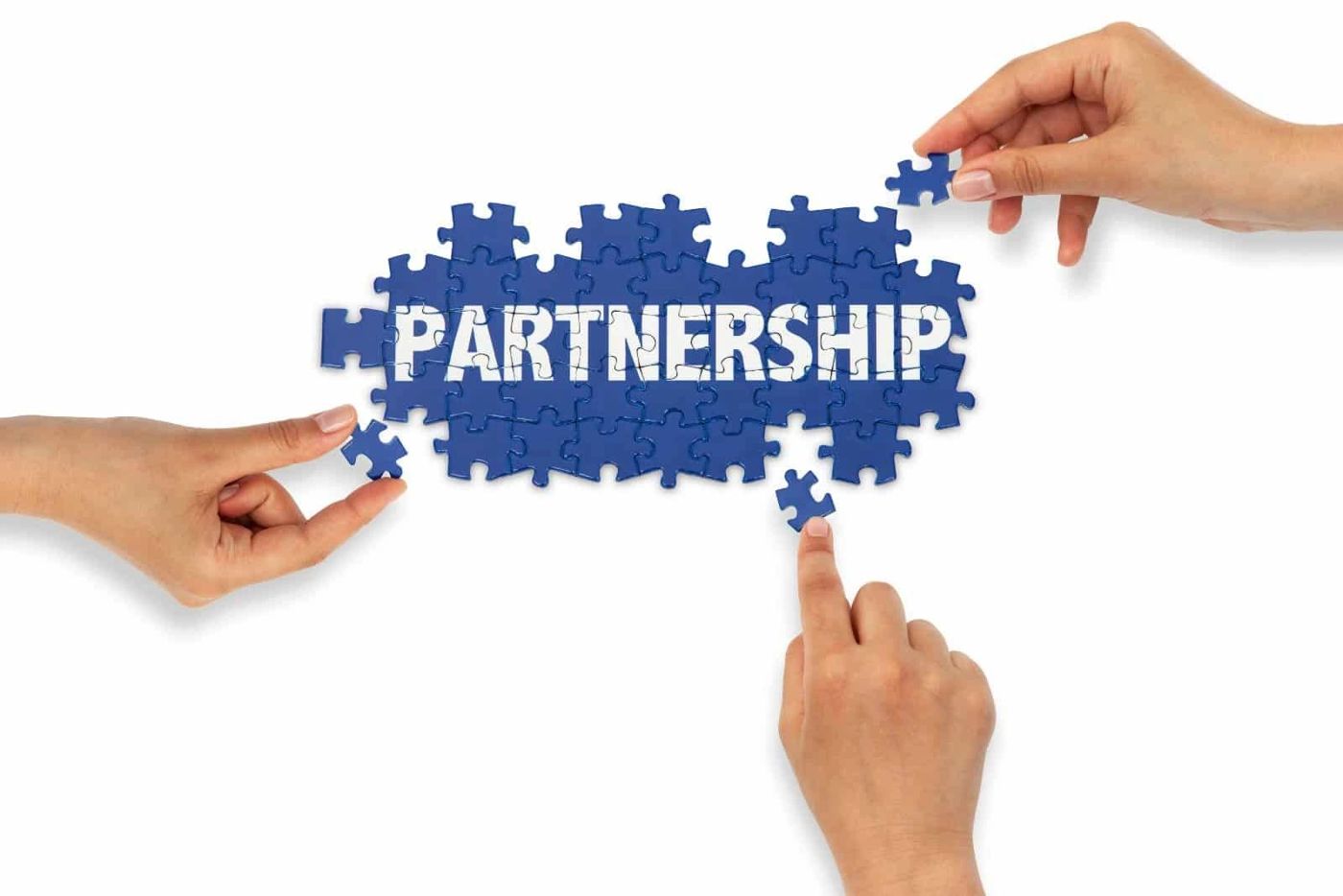 Hands fitting puzzle pieces together to spell Partnership