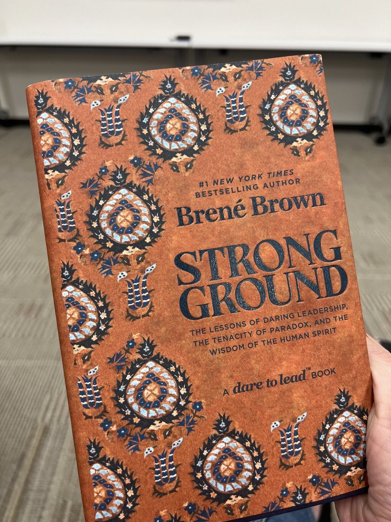 A hand holding a copy of Strong Ground by Brené Brown